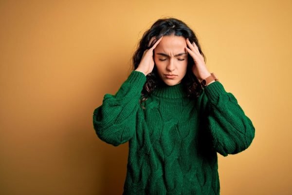 young-beautiful-woman-with-curly-hair-wearing-green-casual-sweater-yellow-background-suffering-from-headache-desperate-stressed-because-pain-migraine-hands-head_839833-28443